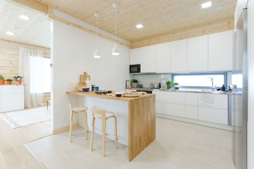 Valkoinen keittiö, kuten kodin kaikki kiintokalusteet, on Kontio Living-mallistoa. K65-jakkarat ja Golden Bell-valaisimet, Artek, Siirtolapuutarha-astiat, Marimekko. Teepannu ja japanilaiset astiat, Tokyokan. Viilu-pärekori ja puukranssi, Verso Design, tarjotin, Mayn.