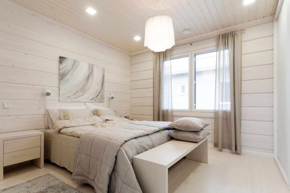 Valkoisen eri sävyjen yhdistely antaa huoneelle syvyyttä ja persoonallisuutta samalla kun hirsiseinä ja luonnonläheiset värit tuovat tilaan lämpöä.